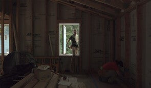 A student stepping through a window in a newly framed house